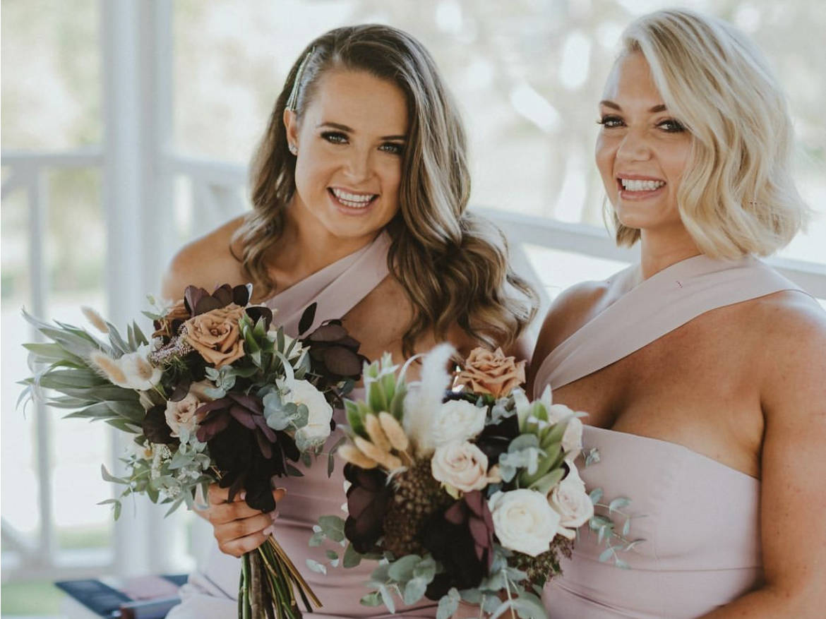 Two bridesmaids with beautiful hair and makeup holding a large bouquet of flowers